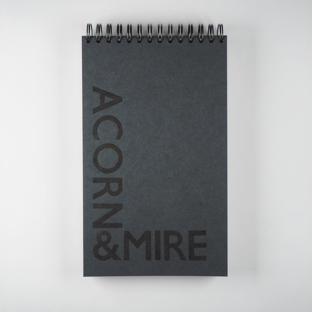 
                  
                    wirebound journal with Acorn & Mire printed with in black wood type on a dark grey cover
                  
                